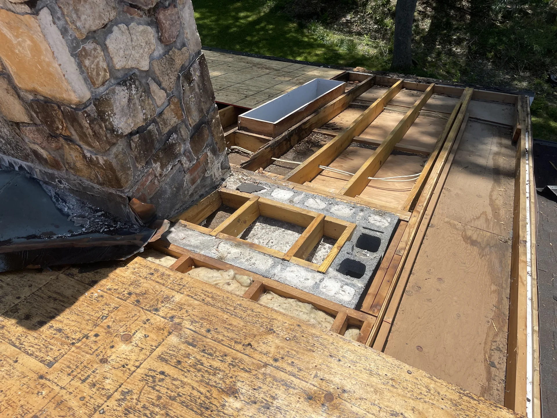 Exposed roof framing and skylight openings beside a stone chimney