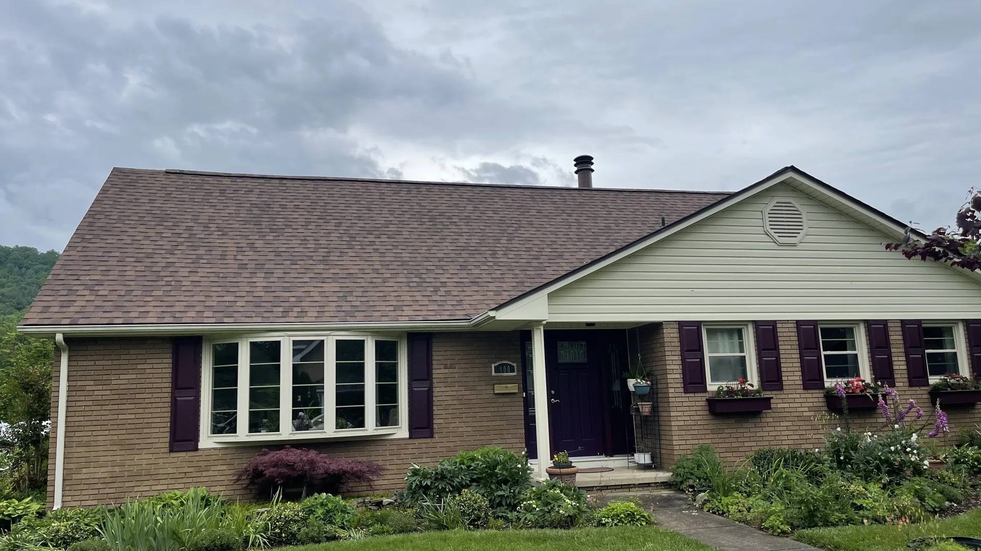 Brick home with a brown shingle roof viewed from the front yard